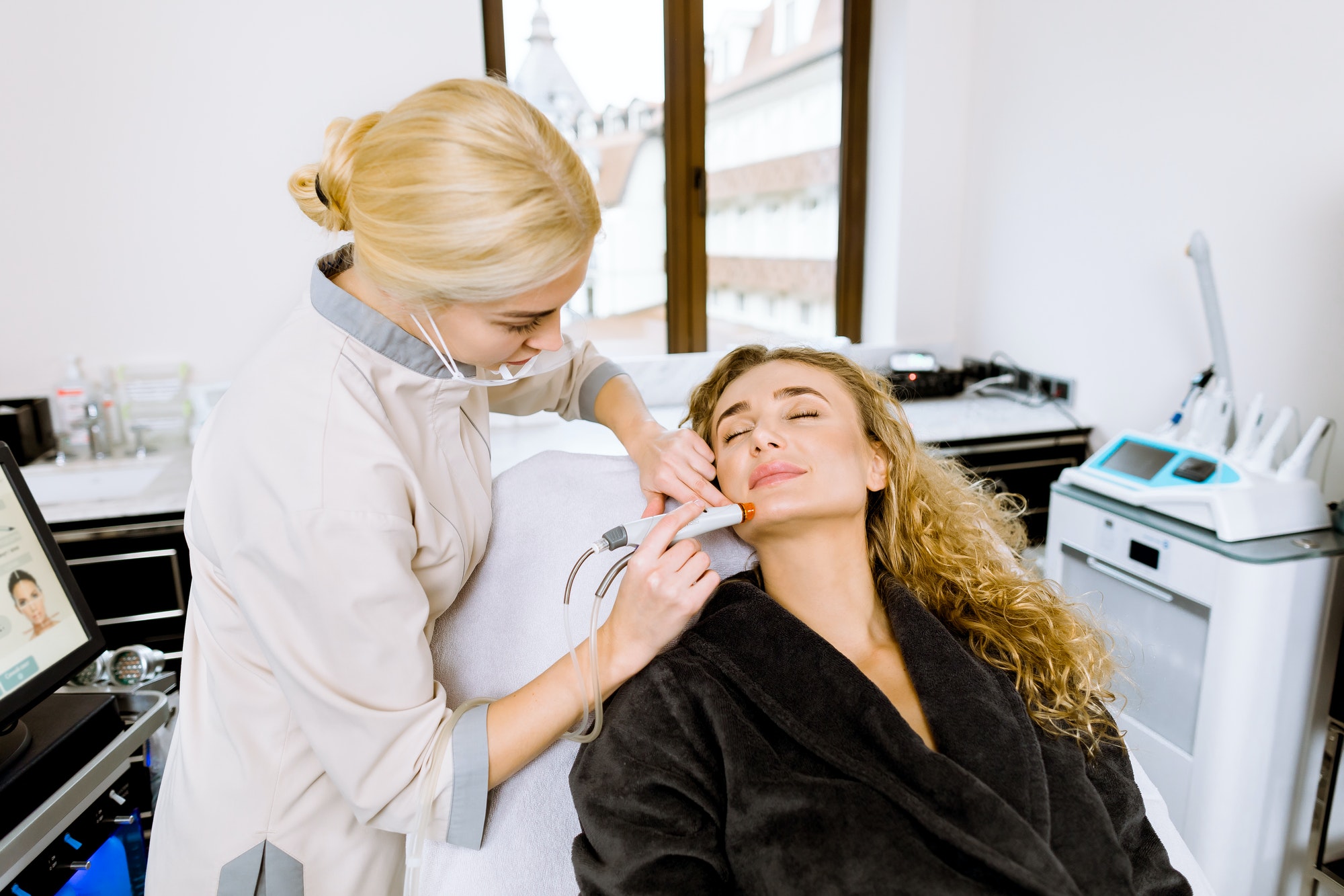Professional young female doctor cosmetologist doing hydrafacial procedure in cosmetology clinic