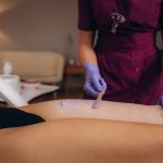 A master applies pink depilatory wax to a young woman's leg for hair removal. Depilation with wax.